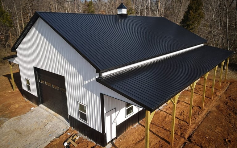 Modern barn with white corrugated walls and dark metal roof, featuring an extended overhang supported by wooden posts in a rural setting